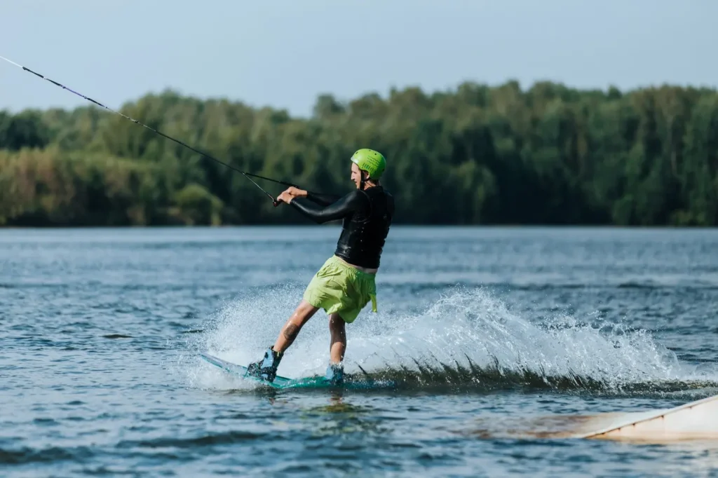Rider sobre uma prancha de wakeboard em manobra atrás do barco em lago ensolarado com respingo d'água