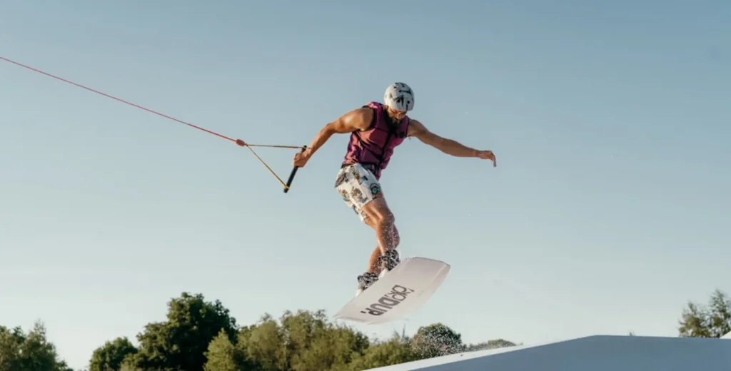 Iniciante no wakeboard se levantando da água com colete salva-vidas em cable park ao sol