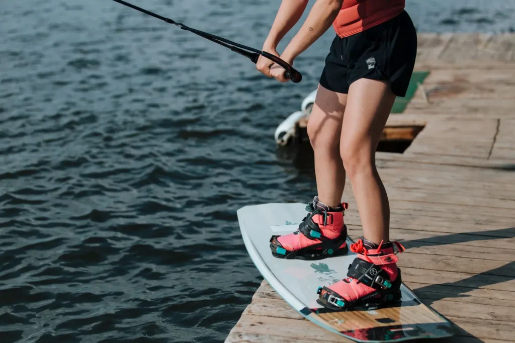 Rider ajustando a bota de wakeboard Ronix Anthem BOA no deck de um cable park antes de entrar na água