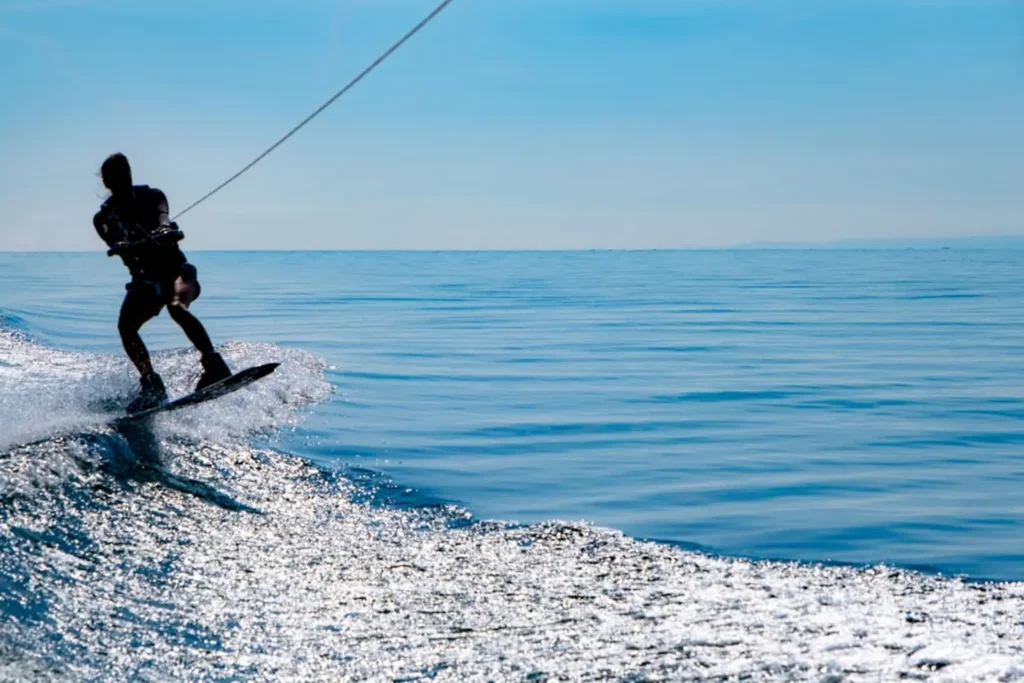 Praticante de wakeboard sendo rebocado por jet ski em lago aberto segurando o cabo da prancha de wakeboard para jet ski