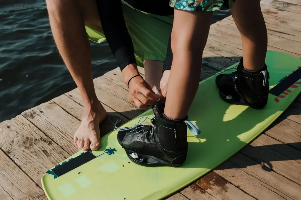 Criança ajustando a wakeboard bindung kids na beira do lago antes de entrar na água para praticar