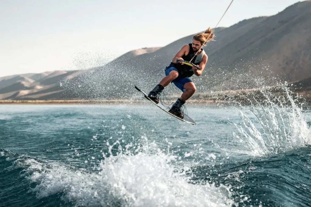 Praticante de wakeboard saltando na wake com prancha durante sessão em lago ensolarado, ilustrando os tipos de prancha de wakeboard