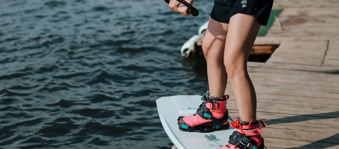 Praticante ajustando bota para prancha de wakeboard na beira de um lago antes da sessão