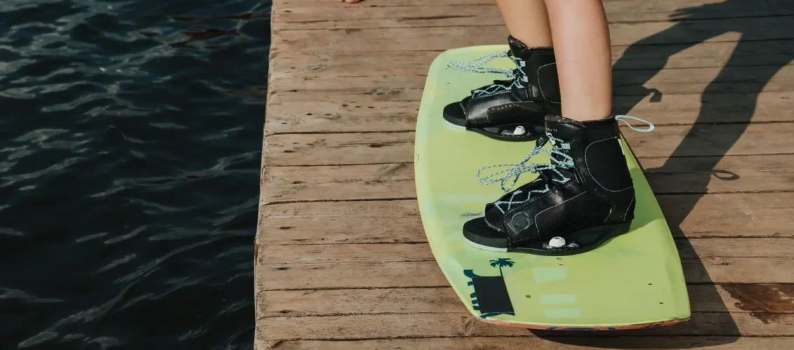 Rider ajustando bota wakeboard Liquid Force na beira do cable park antes de entrar na água