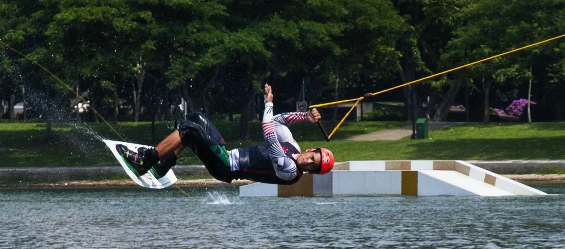 Praticante de wakeboard usando capacete no cable park, deslizando sobre a água em manobra