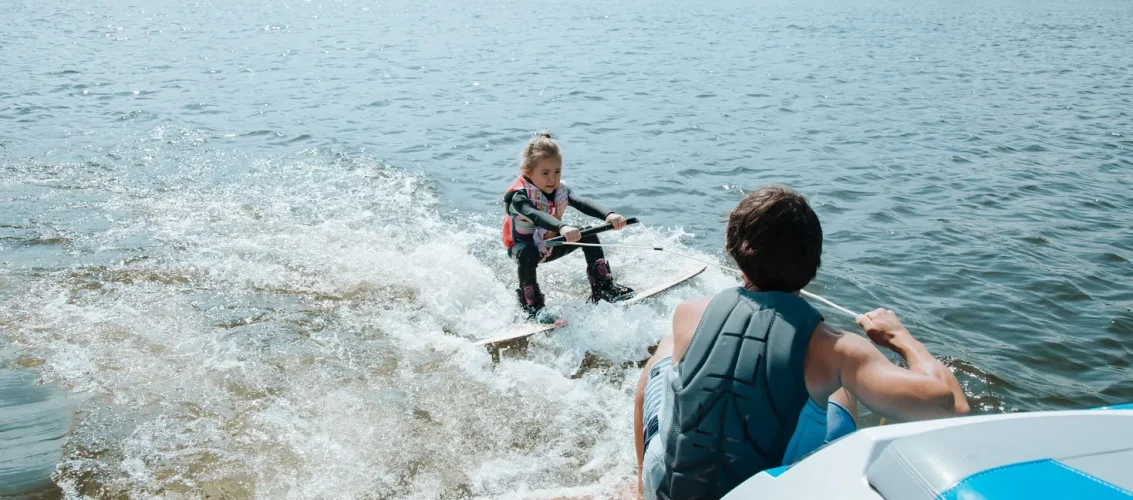Praticante iniciante se levantando na prancha durante sessão de wakeboard puxado por lancha em lago