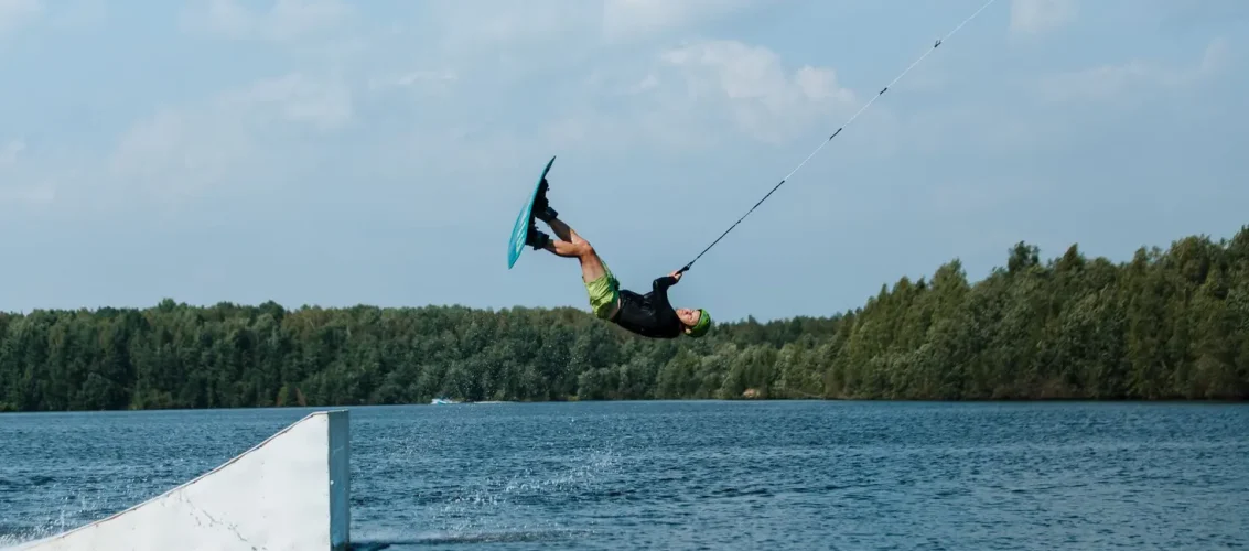 Praticante de wakeboard deslizando sobre lago em cable park em dia ensolarado, demonstrando o que é wakeboard