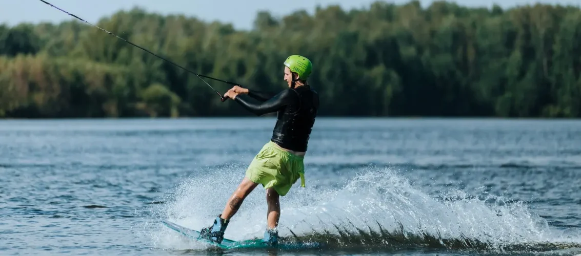 Rider sobre uma prancha de wakeboard em manobra atrás do barco em lago ensolarado com respingo d'água