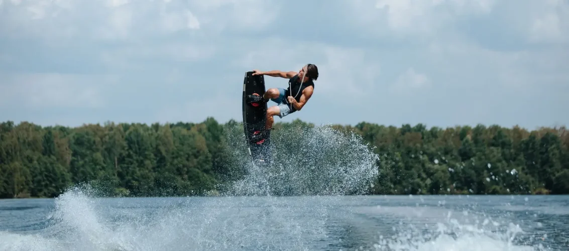 Rider em prancha de wakeboard Sea Doo sendo rebocado por jet ski em lago com água calma