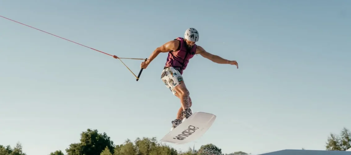 Iniciante no wakeboard se levantando da água com colete salva-vidas em cable park ao sol